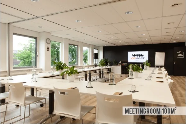 Vergaderruimte van 100 m² met moderne inrichting, grote ramen en U-vormige opstelling.